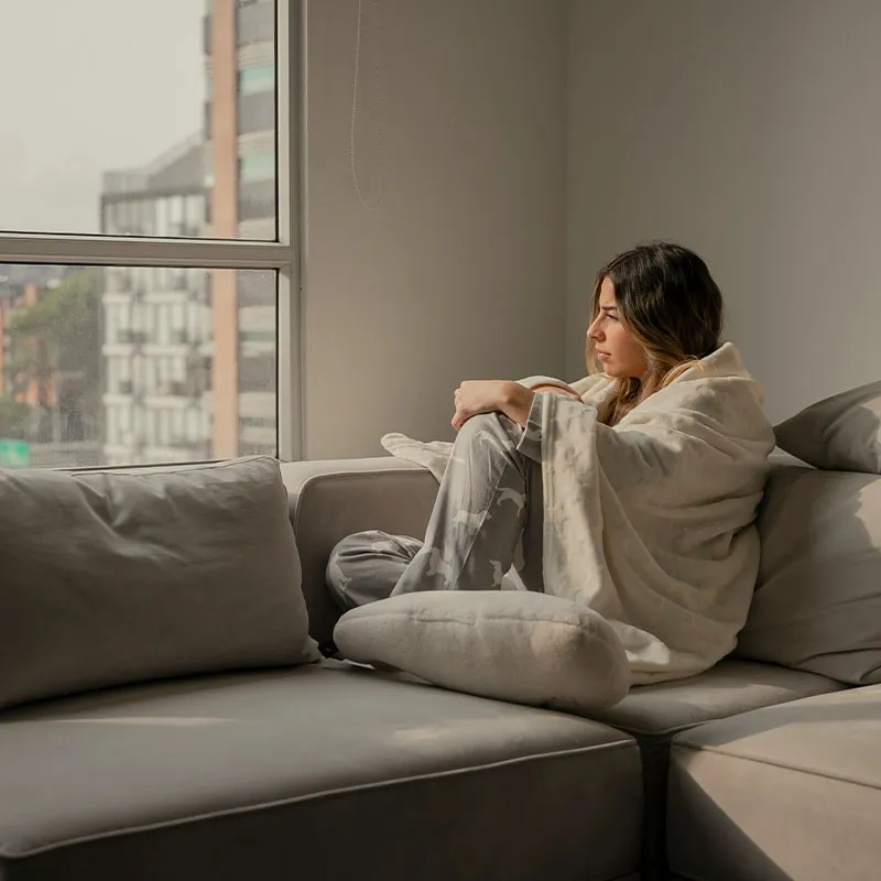 A person sitting wrapped in a blanket, drawn inward and overwhelmed